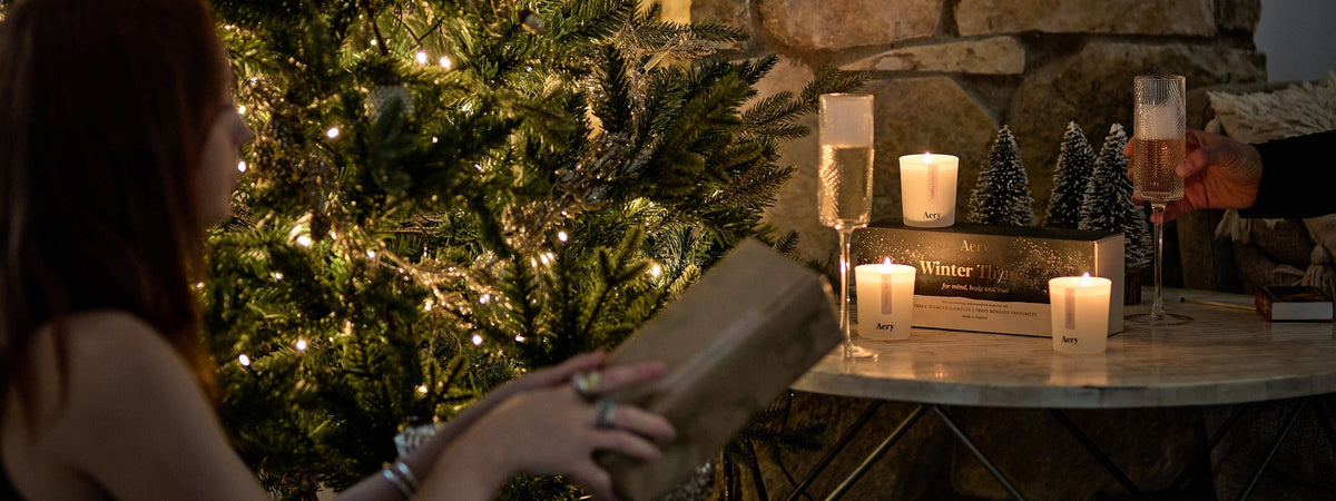 person handing wrapped present to another person infront of a christmas tree