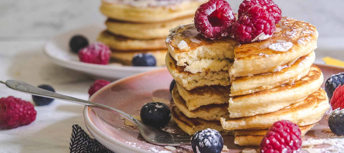 stack of pancakes surrounded by maple syrup, blueberries and raspberries.