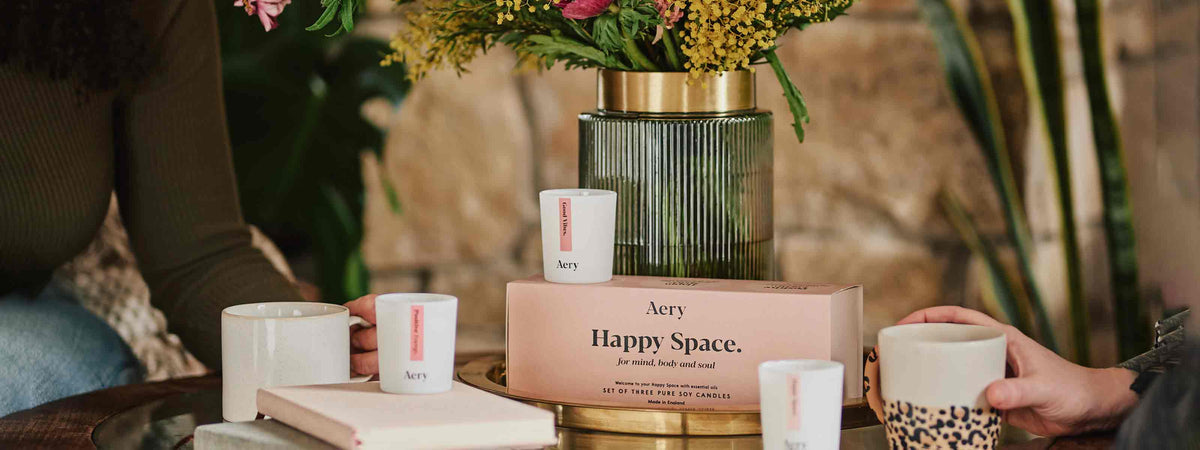 aery living happy space candle gift set next to pink product packaging and bunch of flowers